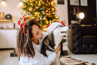 Mutlu bir kadın etrafta hediyelerle Noel ağacının yanında otururken köpeğiyle oynayıp eğleniyor. Kış tatili Yeni Yıl.
