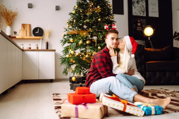 Noel hediyesi değişimi. Genç çift Noel ağacının yakınındaki rahat oturma odasında hediye kutusu açıyor. Romantik bir gün. Kış tatili.