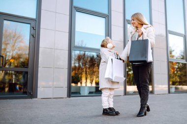 Alışveriş yaptıktan sonra alışveriş torbalarıyla gezen genç bir anne ve sevimli bir çocuk. Kara Cuma. Tüketim, alım, satış, yaşam tarzı, turizm.