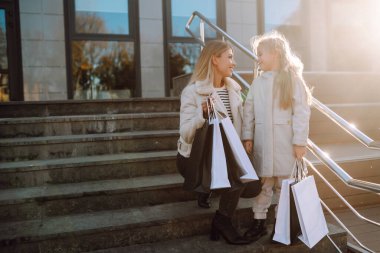 Alışveriş yaptıktan sonra alışveriş torbalarıyla gezen genç bir anne ve sevimli bir çocuk. Kara Cuma. Tüketim, alım, satış, yaşam tarzı, turizm.
