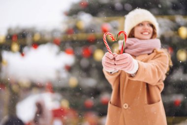 Noel şekerleriyle poz veren mutlu tatlı kadın. Şenlikli çelenk ışıkları. Noel çizgili baston şekerler. Tatlılar.