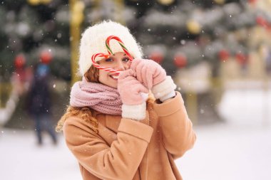 Noel şekerleriyle poz veren mutlu tatlı kadın. Şenlikli çelenk ışıkları. Noel çizgili baston şekerler. Tatlılar.