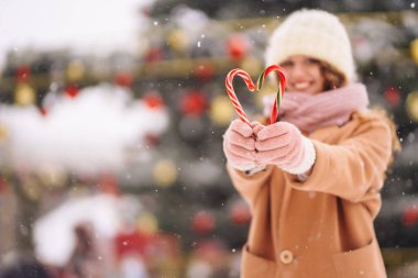 Noel şekerleriyle poz veren mutlu tatlı kadın. Şenlikli çelenk ışıkları. Noel çizgili baston şekerler. Tatlılar.