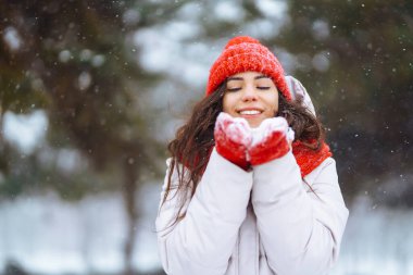 Kışlık kıyafetli genç bir kadın karlı kış gününde dışarıda yürüyor. Doğa, tatiller, dinlenme, seyahat konsepti.