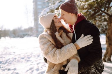Kış ormanlarında yürüyen sevgi dolu genç bir çift. Genç bir adam ve bir kadın dışarıda sarılıp öpüşüyor. Tatiller, mevsimler, aşk ve eğlence kavramı.