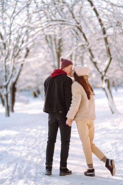 Kış ormanlarında yürüyen sevgi dolu genç bir çift. Genç bir adam ve bir kadın dışarıda sarılıp öpüşüyor. Tatiller, mevsimler, aşk ve eğlence kavramı.