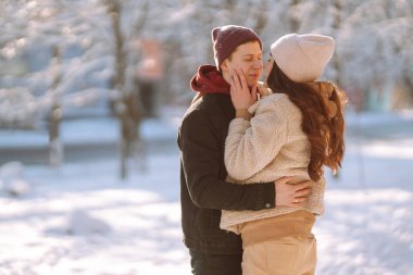 Kış ormanlarında yürüyen sevgi dolu genç bir çift. Genç bir adam ve bir kadın dışarıda sarılıp öpüşüyor. Tatiller, mevsimler, aşk ve eğlence kavramı.