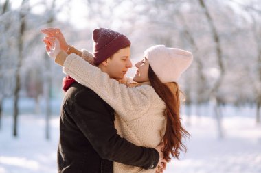 Kış ormanlarında yürüyen sevgi dolu genç bir çift. Genç bir adam ve bir kadın dışarıda sarılıp öpüşüyor. Tatiller, mevsimler, aşk ve eğlence kavramı.