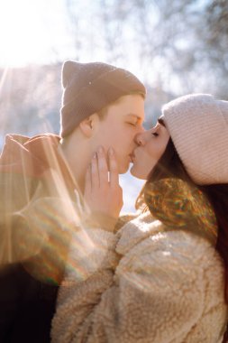 Kış ormanlarında yürüyen sevgi dolu genç bir çift. Genç bir adam ve bir kadın dışarıda sarılıp öpüşüyor. Tatiller, mevsimler, aşk ve eğlence kavramı.