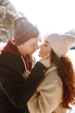 Kış ormanlarında yürüyen sevgi dolu genç bir çift. Genç bir adam ve bir kadın dışarıda sarılıp öpüşüyor. Tatiller, mevsimler, aşk ve eğlence kavramı.