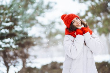Kışın giyinmiş genç bir kadın karlı ormanın arka planına karşı. Doğa, tatiller, dinlenme, seyahat konsepti.