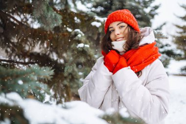 Kışın giyinmiş genç bir kadın karlı ormanın arka planına karşı. Doğa, tatiller, dinlenme, seyahat konsepti.