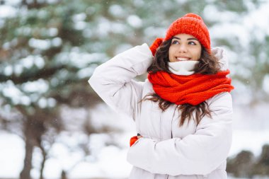 Kışın giyinmiş genç bir kadın karlı ormanın arka planına karşı. Doğa, tatiller, dinlenme, seyahat konsepti.