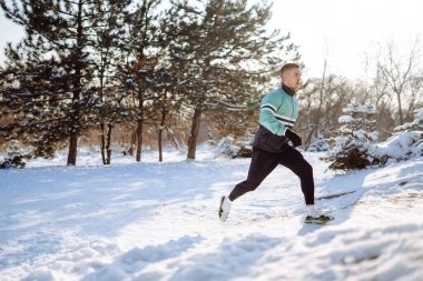 Genç sporcu, güneşli ve karlı kış gününde ormanda egzersiz yapıyor. Açık hava fitness, kardiyo egzersizleri, kış fitness, aktif yaşam..