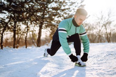 Genç sporcu, güneşli ve karlı kış gününde ormanda egzersiz yapıyor. Açık hava fitness, kardiyo egzersizleri, kış fitness, aktif yaşam..