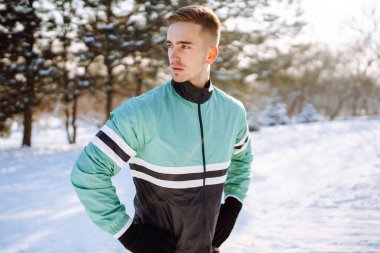 Genç sporcu, güneşli ve karlı kış gününde ormanda egzersiz yapıyor. Açık hava fitness, kardiyo egzersizleri, kış fitness, aktif yaşam..