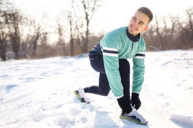 Genç sporcu, güneşli ve karlı kış gününde ormanda egzersiz yapıyor. Açık hava fitness, kardiyo egzersizleri, kış fitness, aktif yaşam..