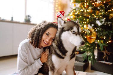 Kış tatilini Noel ağacının arkasında Husky köpeğiyle kutlayan mutlu bir kadın. Yeni yıl. Noel sürprizi.