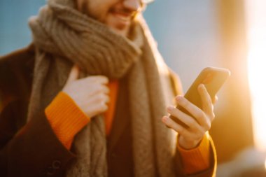 Hat bağlantısı. Kışlık giysiler içindeki genç adam sokakta yürüyor, telefonuna bakıyor ve mesaj yolluyor. İş konsepti