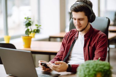 Yaratıcı adam ekranda akıllı telefonla mesaj yazmaya çalışıyor. Laptop kullanarak rahatlayan genç adam bilgisayar çalışıyor ve video konferansı yapıyor. İş konsepti.