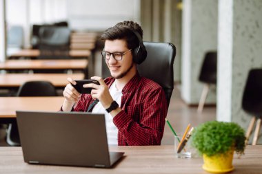 Yaratıcı adam ekranda akıllı telefonla mesaj yazmaya çalışıyor. Laptop kullanarak rahatlayan genç adam bilgisayar çalışıyor ve video konferansı yapıyor. İş konsepti.