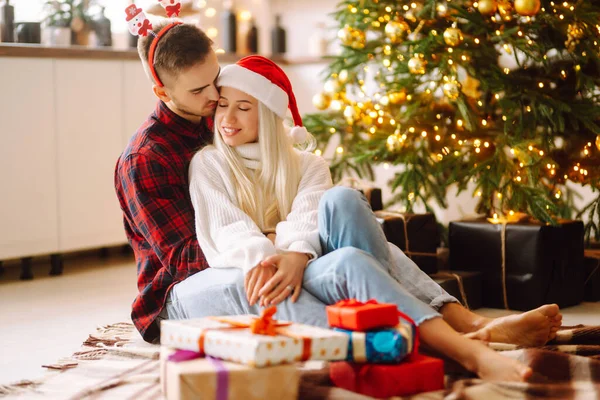 クリスマスツリーの近くの家でクリスマスプレゼントを持つ若いカップル ロマンチックな日だ 冬休みだ — ストック写真