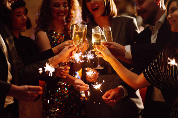 Sparkling sparklers in the hands of young friends. People  celebrate winter holidays with sparkles and champagne. Holidays, vacation, relax, party and lifestyle concept.
