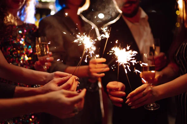 Genç arkadaşlarının ellerinde kıvılcımlar saçıyor. İnsanlar kış tatillerini ışıltı ve şampanyayla kutlar. Tatil, tatil, rahatlama, parti ve yaşam tarzı konsepti.