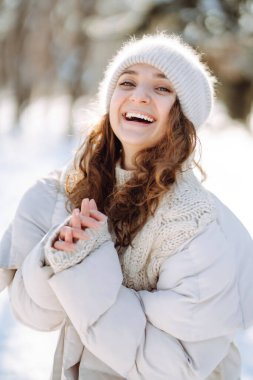 Young woman in winter style clothes walking in the snowy park. Winter fashion, holidays, nature,  travel concept.