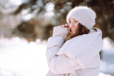 Young woman in winter style clothes walking in the snowy park. Winter fashion, holidays, nature,  travel concept.