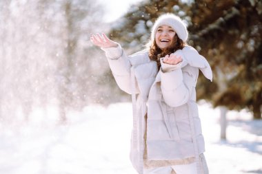 Young woman in winter style clothes walking in the snowy park. Winter fashion, holidays, nature,  travel concept.