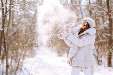 Young woman in winter style clothes walking in the snowy park. Winter fashion, holidays, nature,  travel concept.