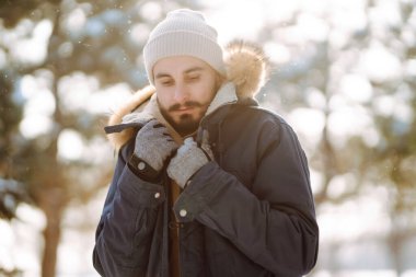 Handsome bearded young  man standing outdoors fur hood in winter season forest. Season holiday leisure. Nature.