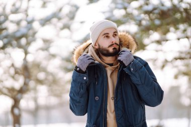 Handsome bearded young  man standing outdoors fur hood in winter season forest. Season holiday leisure. Nature.