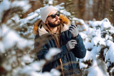 Handsome bearded young  man standing outdoors fur hood in winter season forest. Season holiday leisure. Nature.