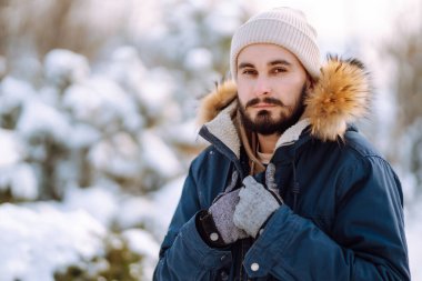 Handsome bearded young  man standing outdoors fur hood in winter season forest. Season holiday leisure. Nature.