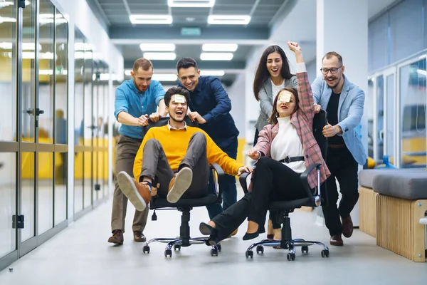 Jóvenes Alegres Empresarios Divierten Mientras Corren Sillas Oficina Sonríen Amistoso —  Fotos de Stock