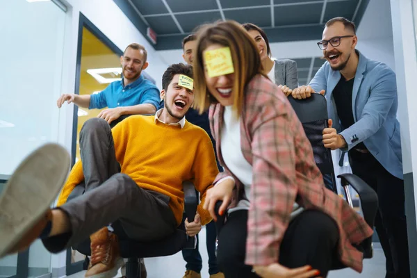 Jóvenes Alegres Empresarios Divierten Mientras Corren Sillas Oficina Sonríen Amistoso —  Fotos de Stock