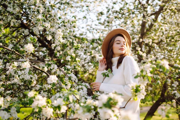 Çiçek açan bahar bahçesinde kokunun tadını çıkaran genç bir kadın. Rahatlama, seyahat, özgürlük ve bahar tatili kavramı. Moda tarzı