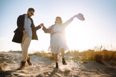 Deniz kenarında yürüyen ve kucaklaşan şık bir çift. İlkbahar. Rahatlama, gençlik, aşk, doğayla baş başa yaşam tarzı.