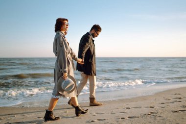 Deniz kenarında yürüyen ve kucaklaşan şık bir çift. İlkbahar. Rahatlama, gençlik, aşk, doğayla baş başa yaşam tarzı.