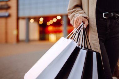 Alışveriş merkezinin yakınında alışveriş torbaları olan genç bir kadın. Bahar stili. Tüketim, satın alma, alışveriş, yaşam tarzı, satış kavramı.