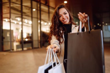 Alışveriş merkezinin yakınında alışveriş torbaları olan genç bir kadın. Bahar stili. Tüketim, satın alma, alışveriş, yaşam tarzı, satış kavramı.