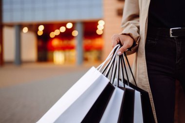 Alışveriş merkezinin yakınında alışveriş torbaları olan genç bir kadın. Bahar stili. Tüketim, satın alma, alışveriş, yaşam tarzı, satış kavramı.