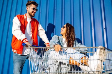 Şık bir erkek ve kadın eğleniyor ve alışveriş arabasına biniyor. Yaşam tarzı, eğlence, eğlence, gençlik kavramı.