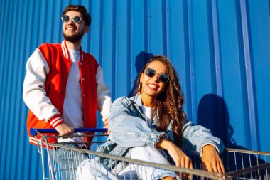Şık bir erkek ve kadın eğleniyor ve alışveriş arabasına biniyor. Yaşam tarzı, eğlence, eğlence, gençlik kavramı.