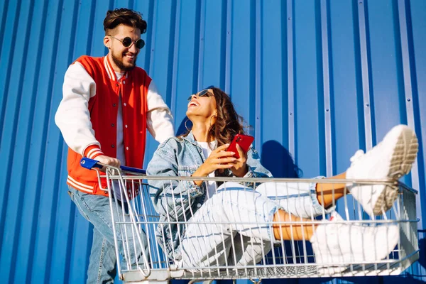 Şık bir erkek ve kadın eğleniyor ve alışveriş arabasına biniyor. Yaşam tarzı, eğlence, eğlence, gençlik kavramı.
