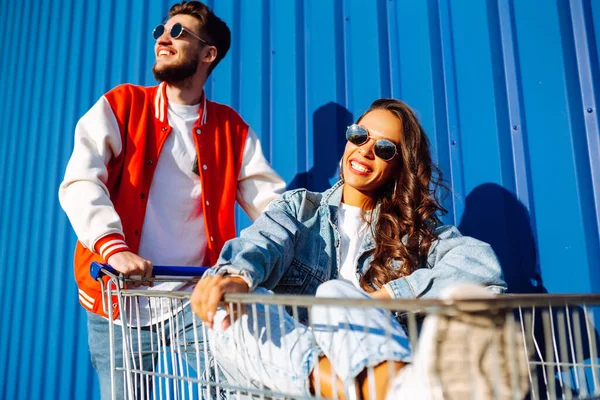 Şık bir erkek ve kadın eğleniyor ve alışveriş arabasına biniyor. Yaşam tarzı, eğlence, eğlence, gençlik kavramı.