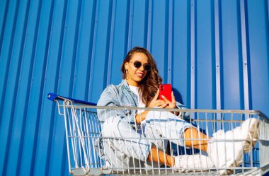 Selfie zamanı. Genç bir kadın alışveriş arabalarında eğleniyor. Tüketim, satış, indirimler, yaşam tarzı konsepti.