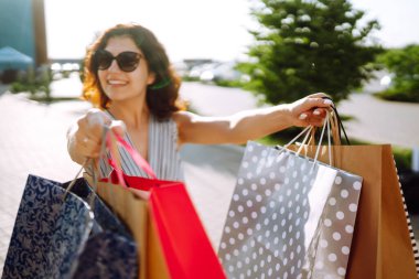 Alışveriş zamanı. Alışveriş merkezinin yakınında alışveriş torbaları taşıyan genç bir kadın. Tüketim, satış, alım satım, alışveriş, yaşam tarzı konsepti. Yaz.